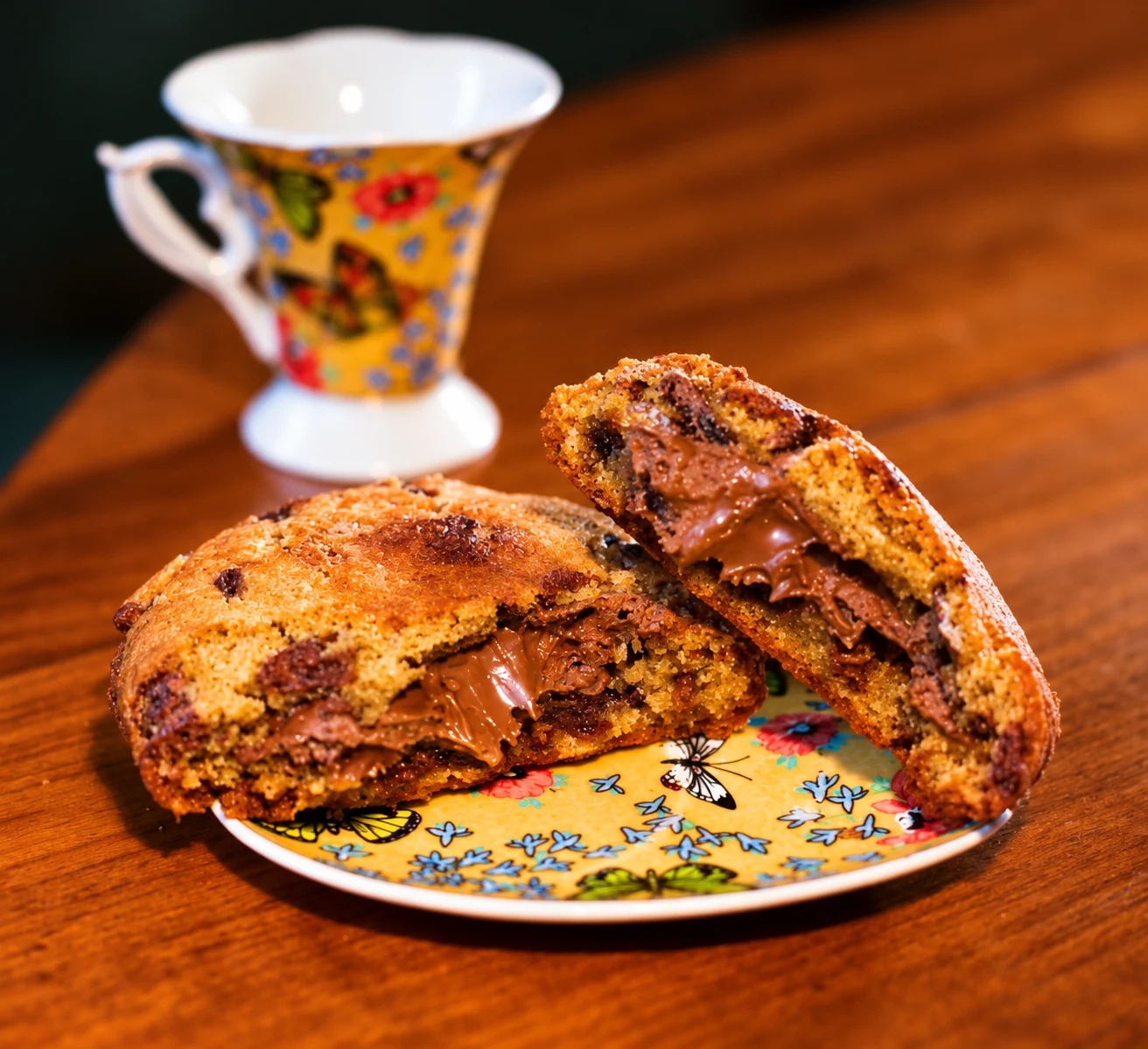 Cookie recheado de Nutella partido ao meio, com uma xícara ao fundo